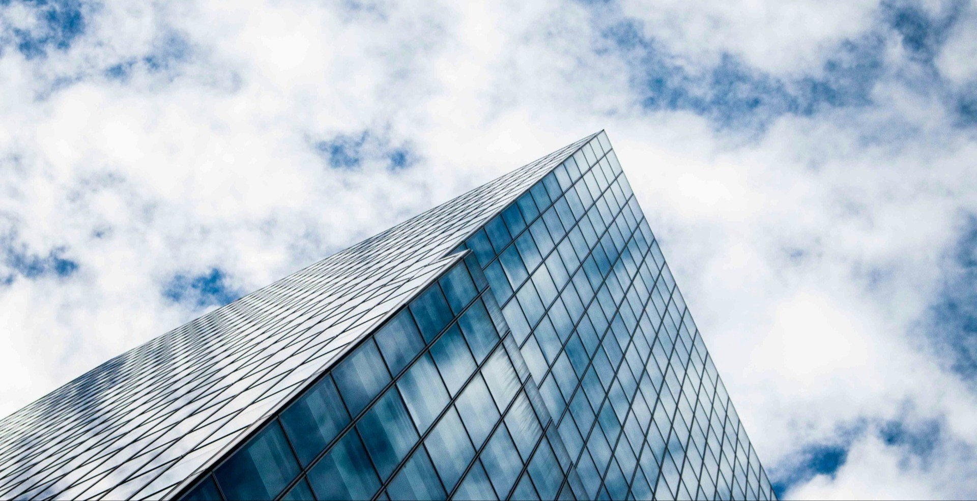 peak of a glass office building with cloudy blue sky